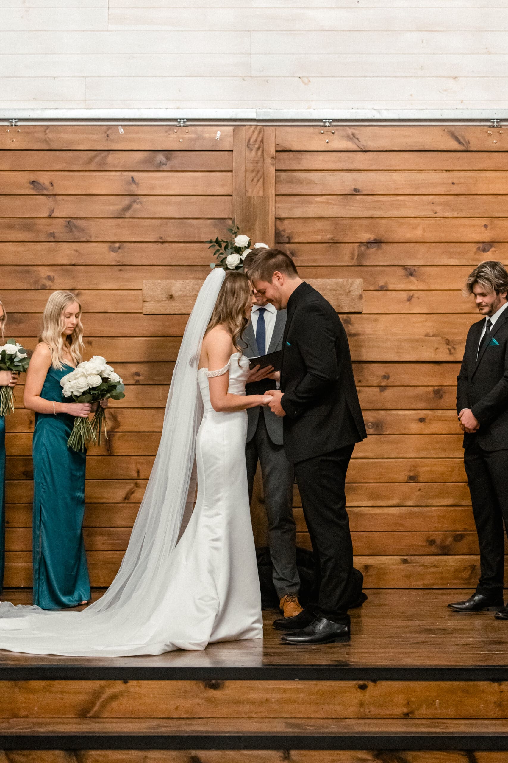 Bride and groom holding hands and praying during their winter wedding ceremony at The Silver Spoon Barn