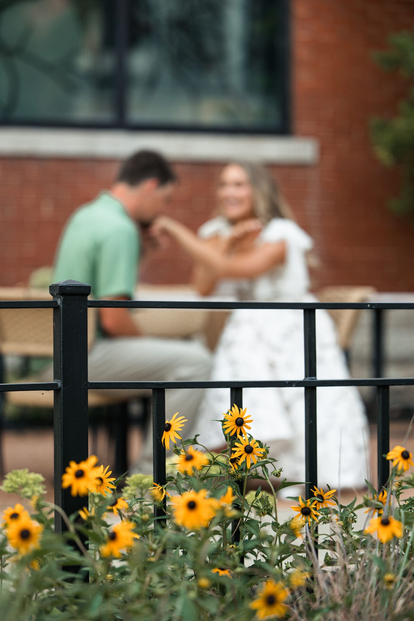 Groom kisses bride’s hand while they sit at a romantic table together. Wichita Engagement Photographer