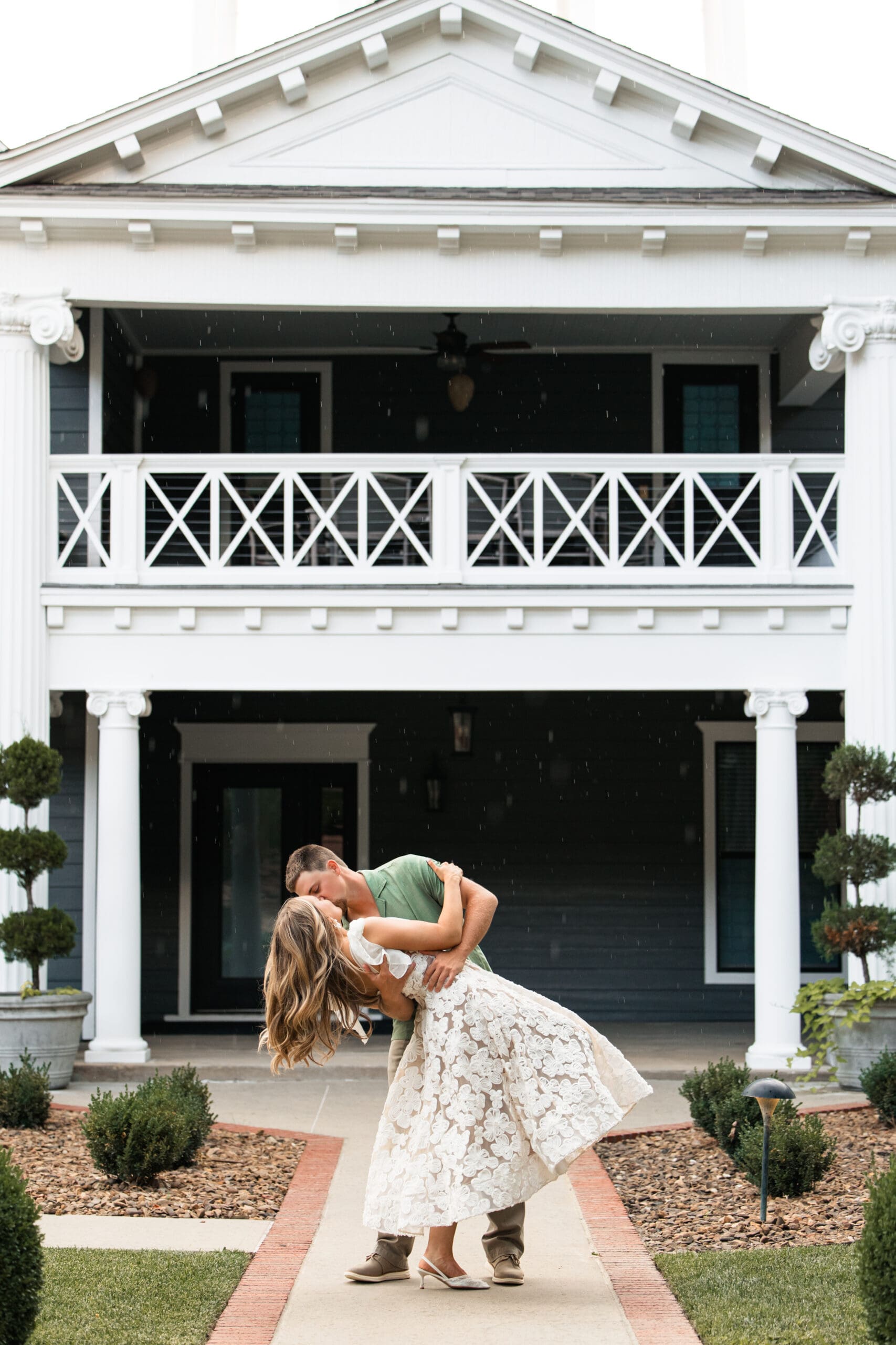 Dramatic dip kiss in front of a charming Southern-style house. Wichita Engagement Photographer