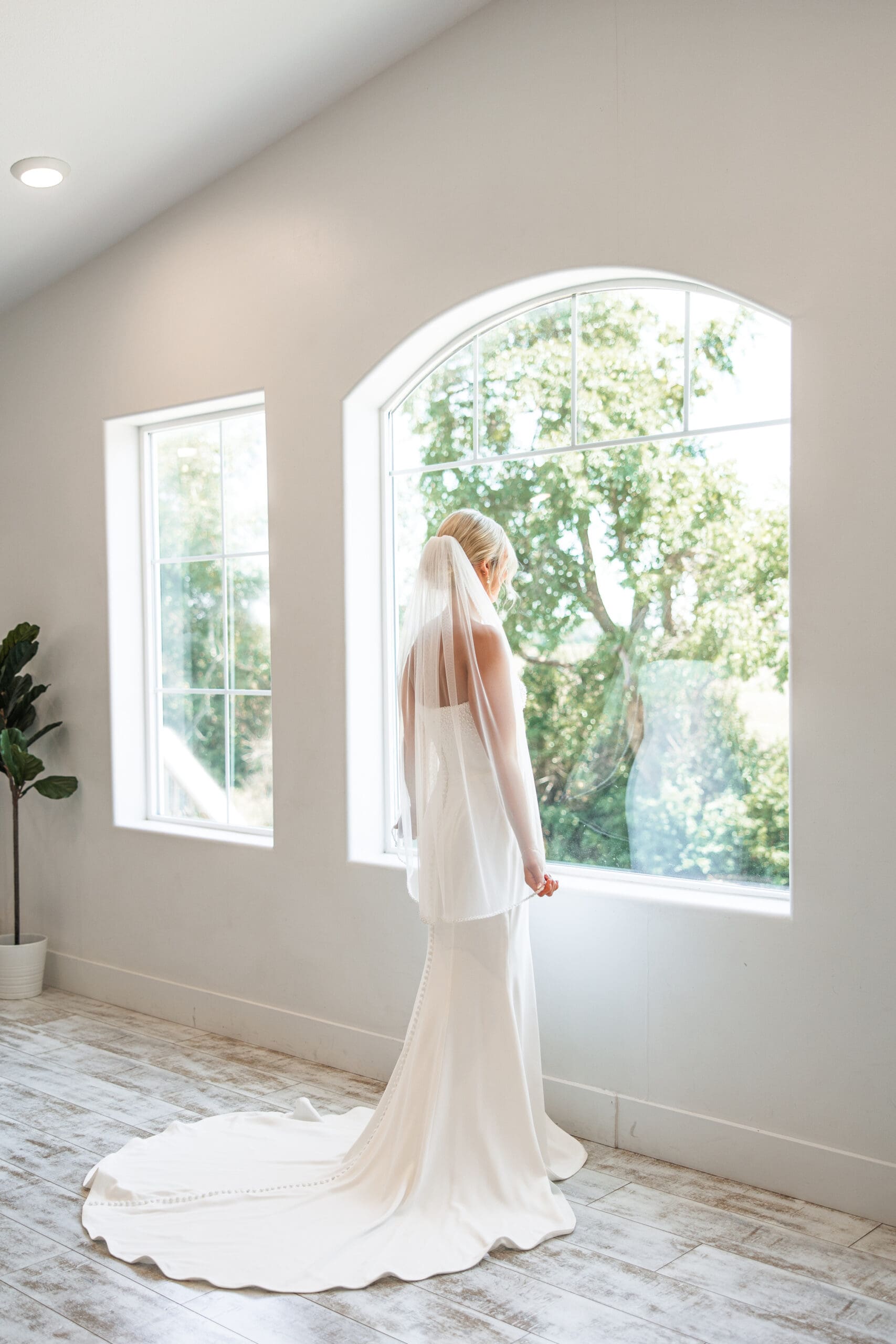 Bride in dress and veil looking out window 