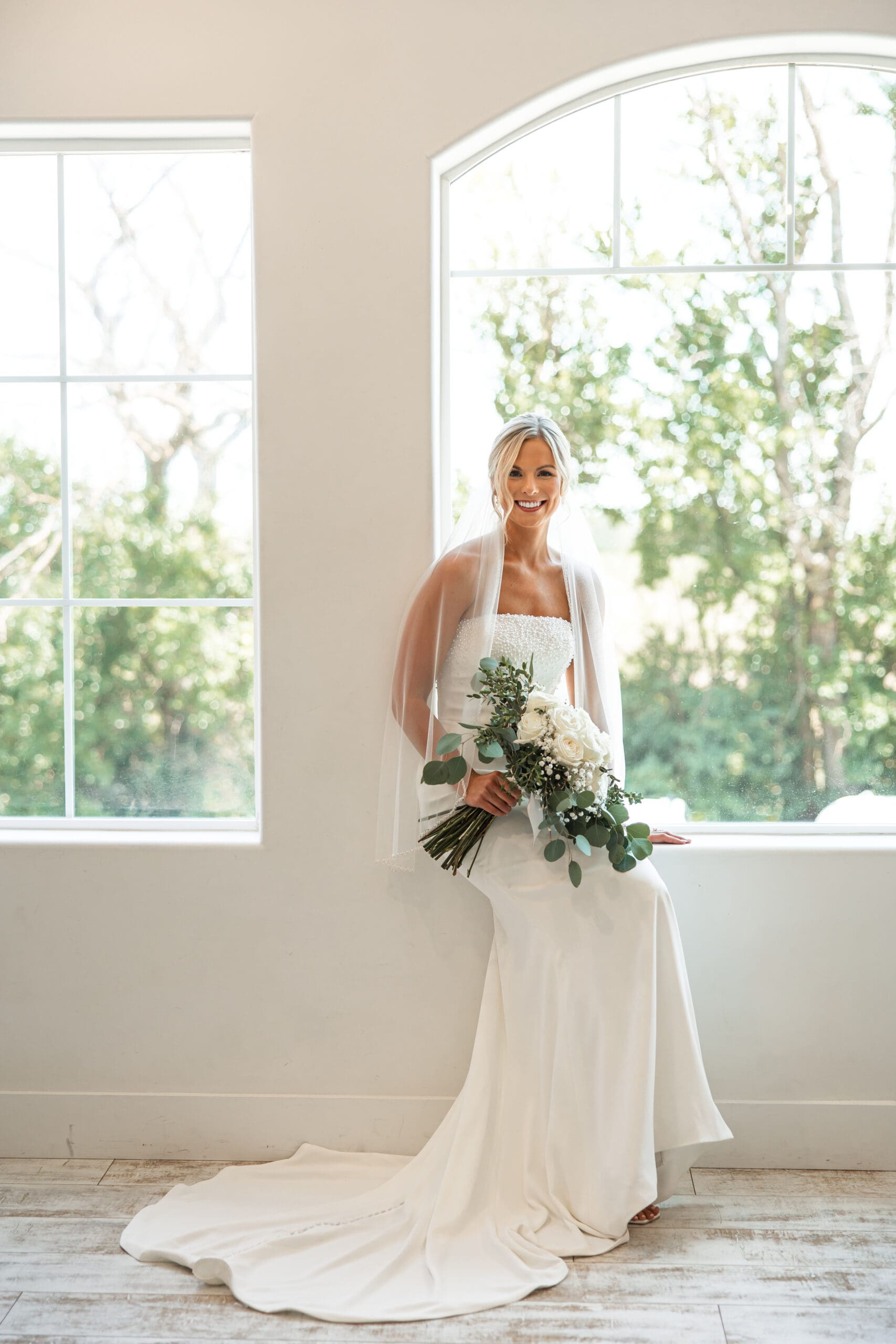 Bride sitting in windowsill holding bouquet 
