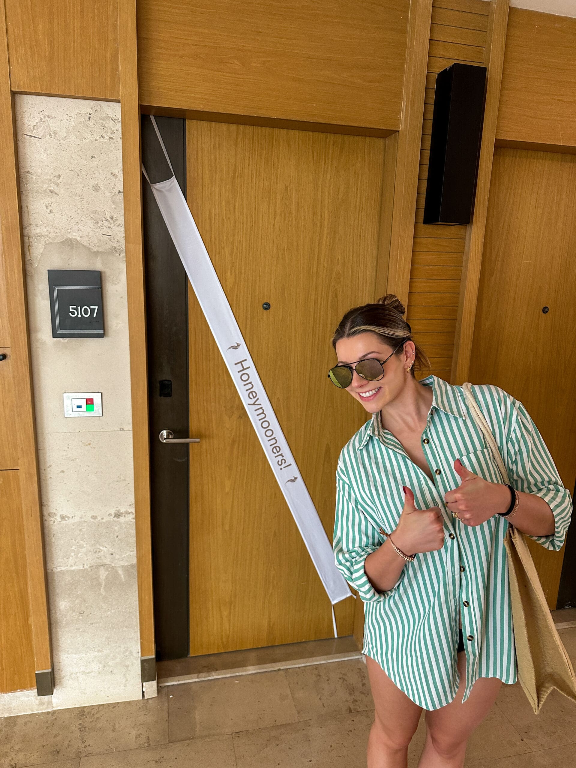 Smiling honeymoon couple in front of their room with “Honeymooners” sign