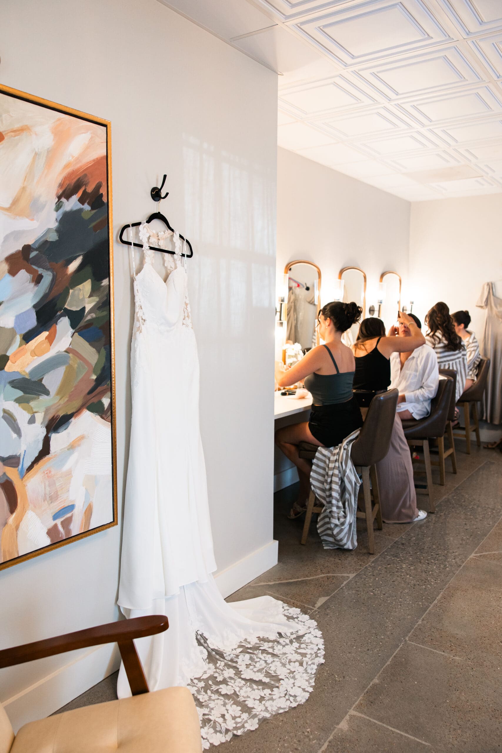 Bride’s gown hanging beside bridesmaids getting ready at Stone Manor on 79th, captured by Wichita wedding photographer.