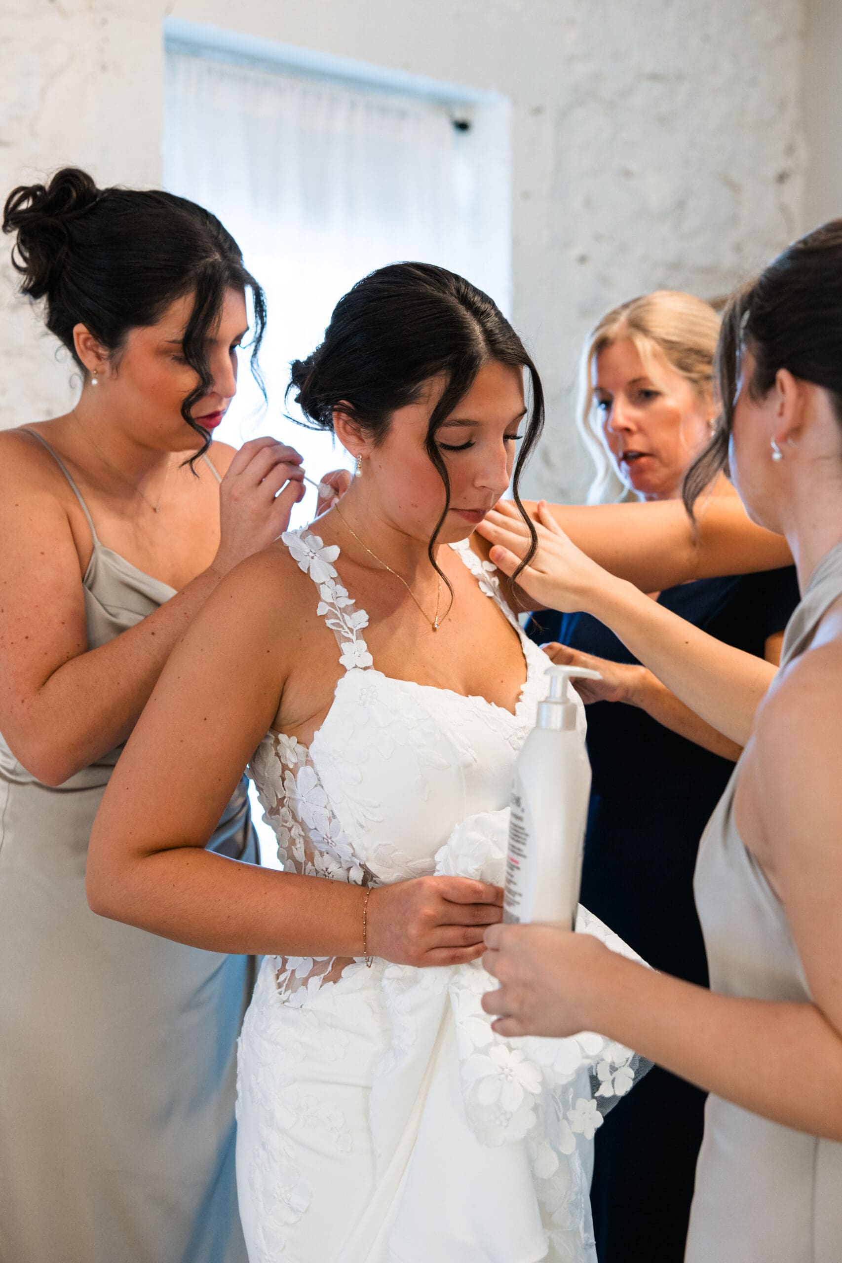 Bridesmaids buttoning the bride’s lace gown before the wedding ceremony at Stone Manor on 79th in Overland Park, Kansas.