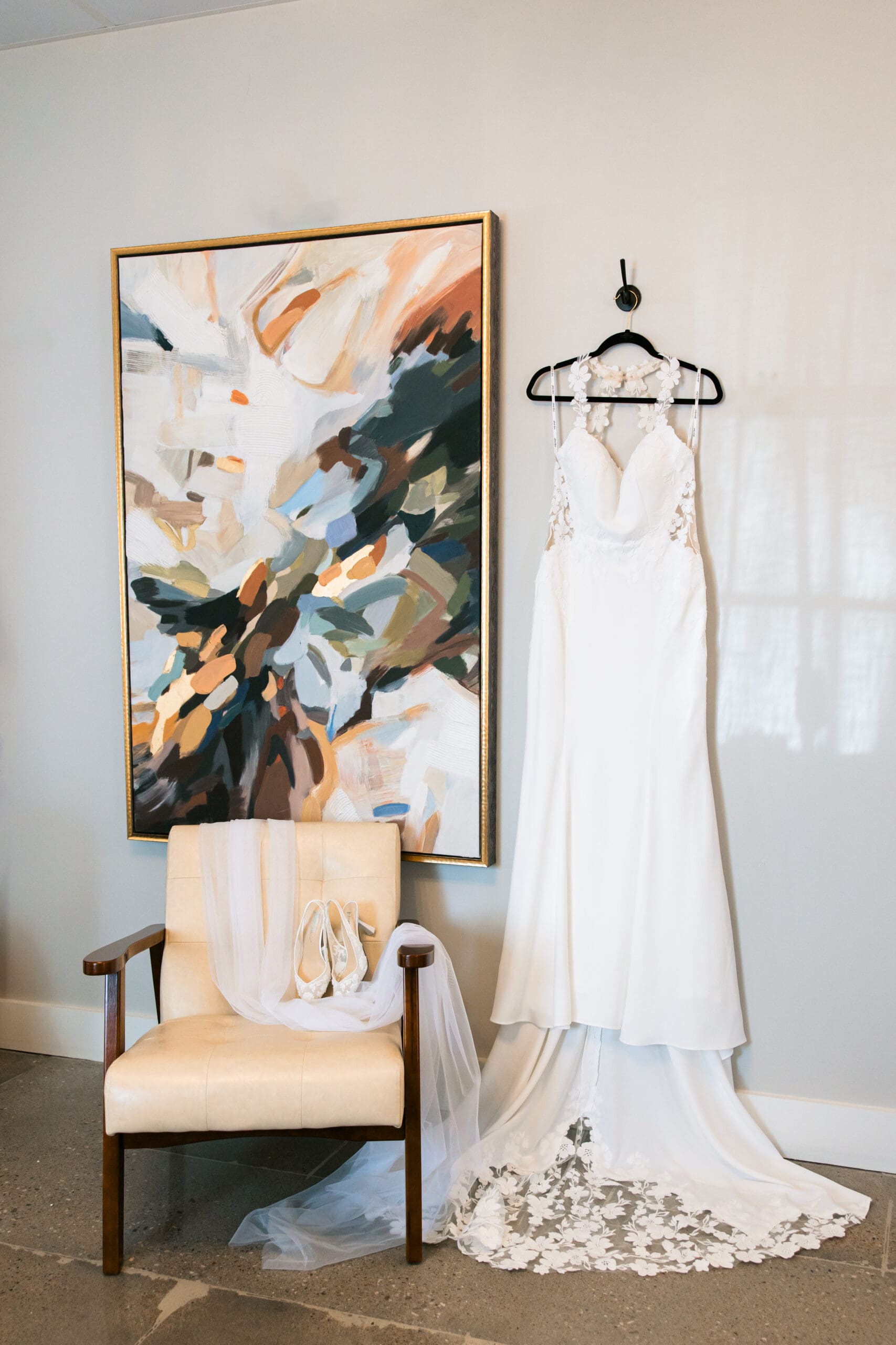 Bride’s lace wedding gown and veil hanging beside a modern painting at Stone Manor on 79th in Overland Park, Kansas.