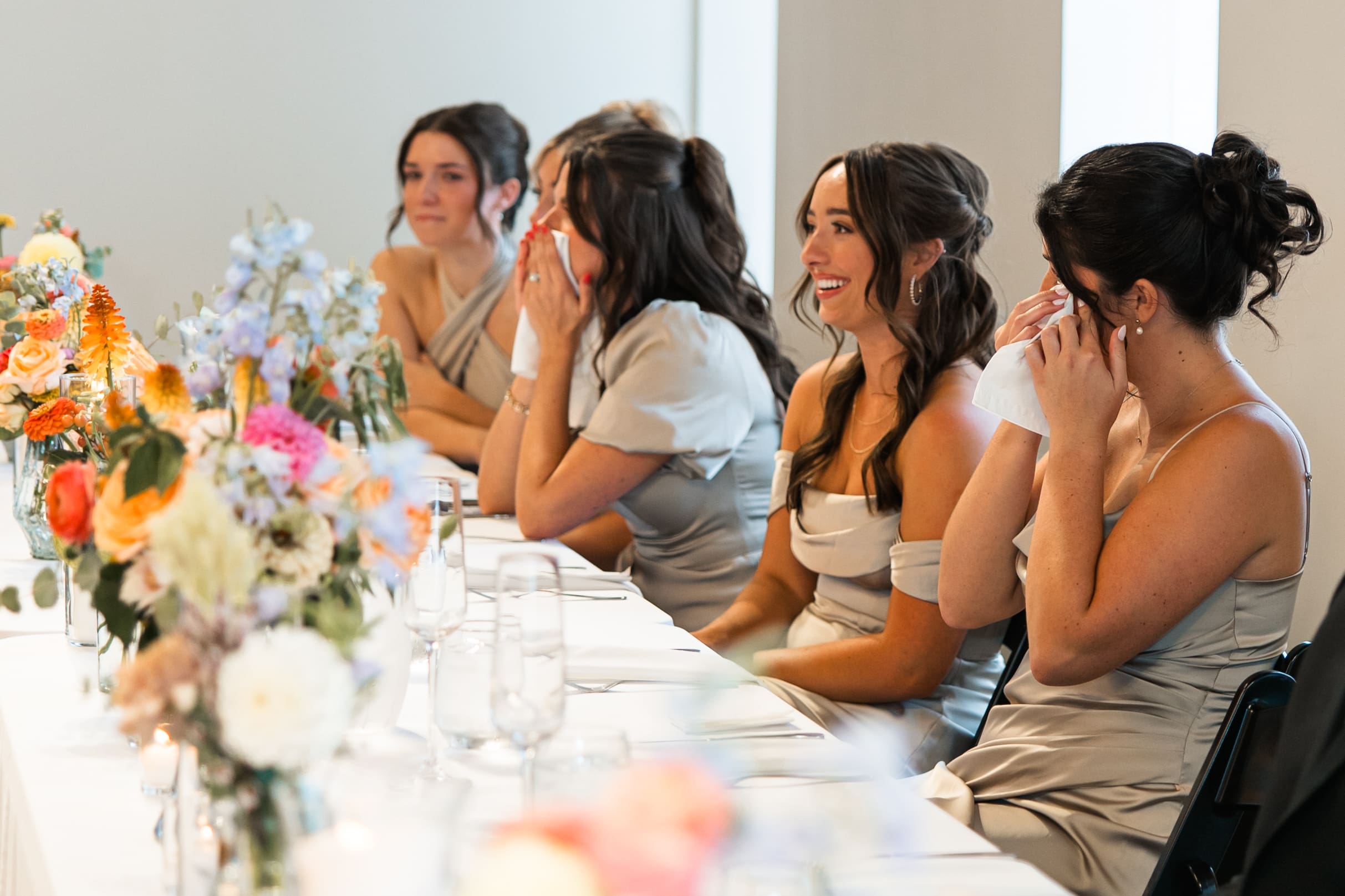 Bridesmaids laugh and wipe away tears during wedding speeches at Stone Manor on 79th in Overland Park, Kansas.
