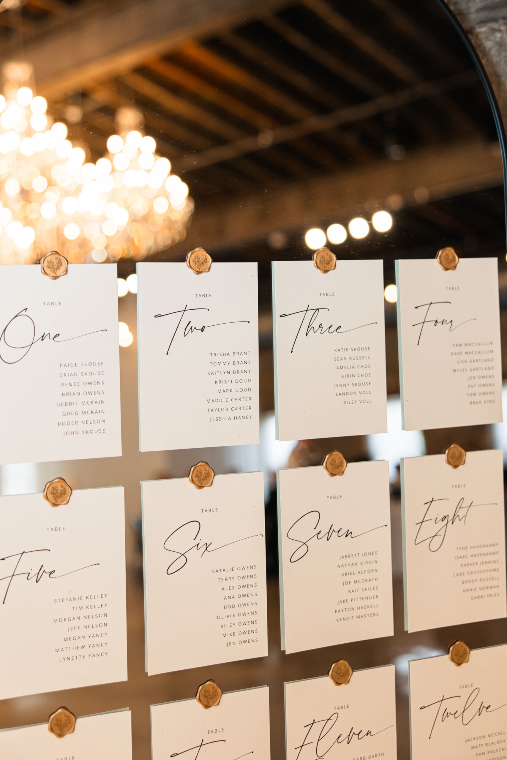 Elegant wedding seating chart with wax seals displayed on a mirror under chandeliers at Stone Manor on 79th in Overland Park, Kansas.