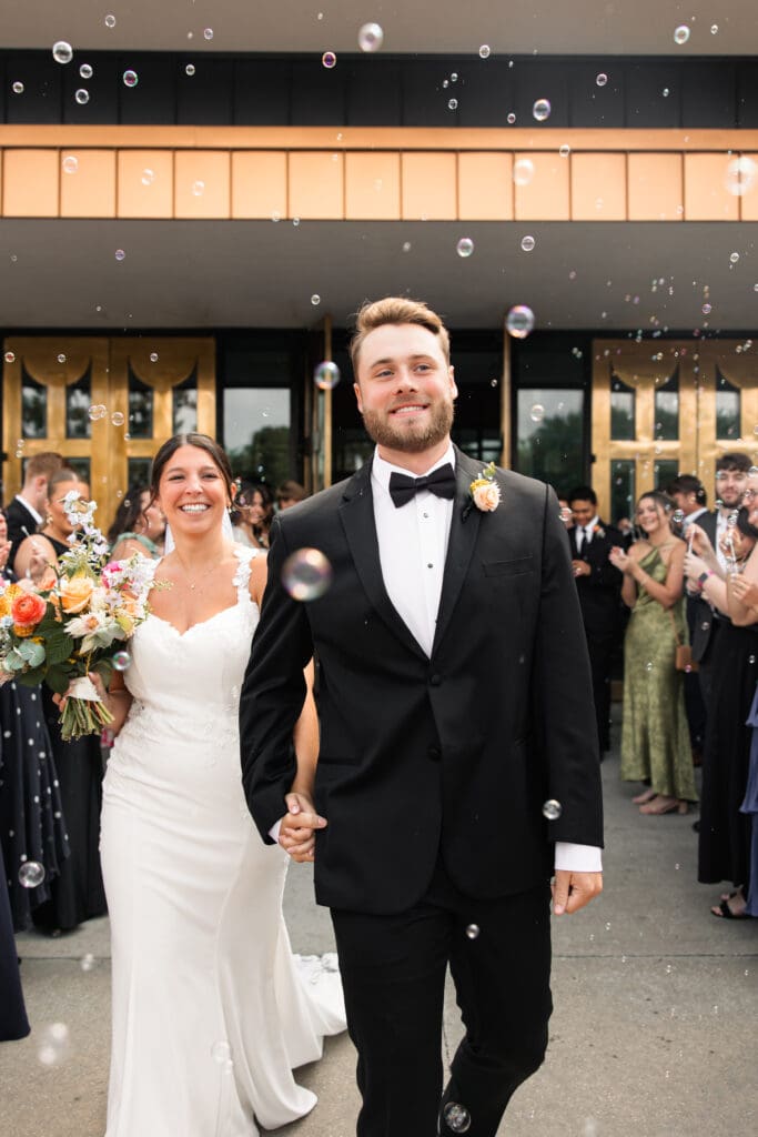 Newlyweds walking hand-in-hand through bubbles after their ceremony at Holy Spirit Catholic Parish in Overland Park, celebrating their Kansas wedding day.
