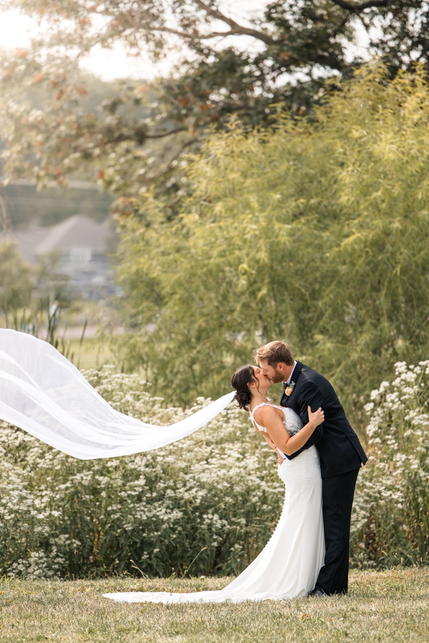 Romantic bride and groom kiss with veil floating in the breeze at golden hour in Meadowbrook Park, Overland Park, Kansas.