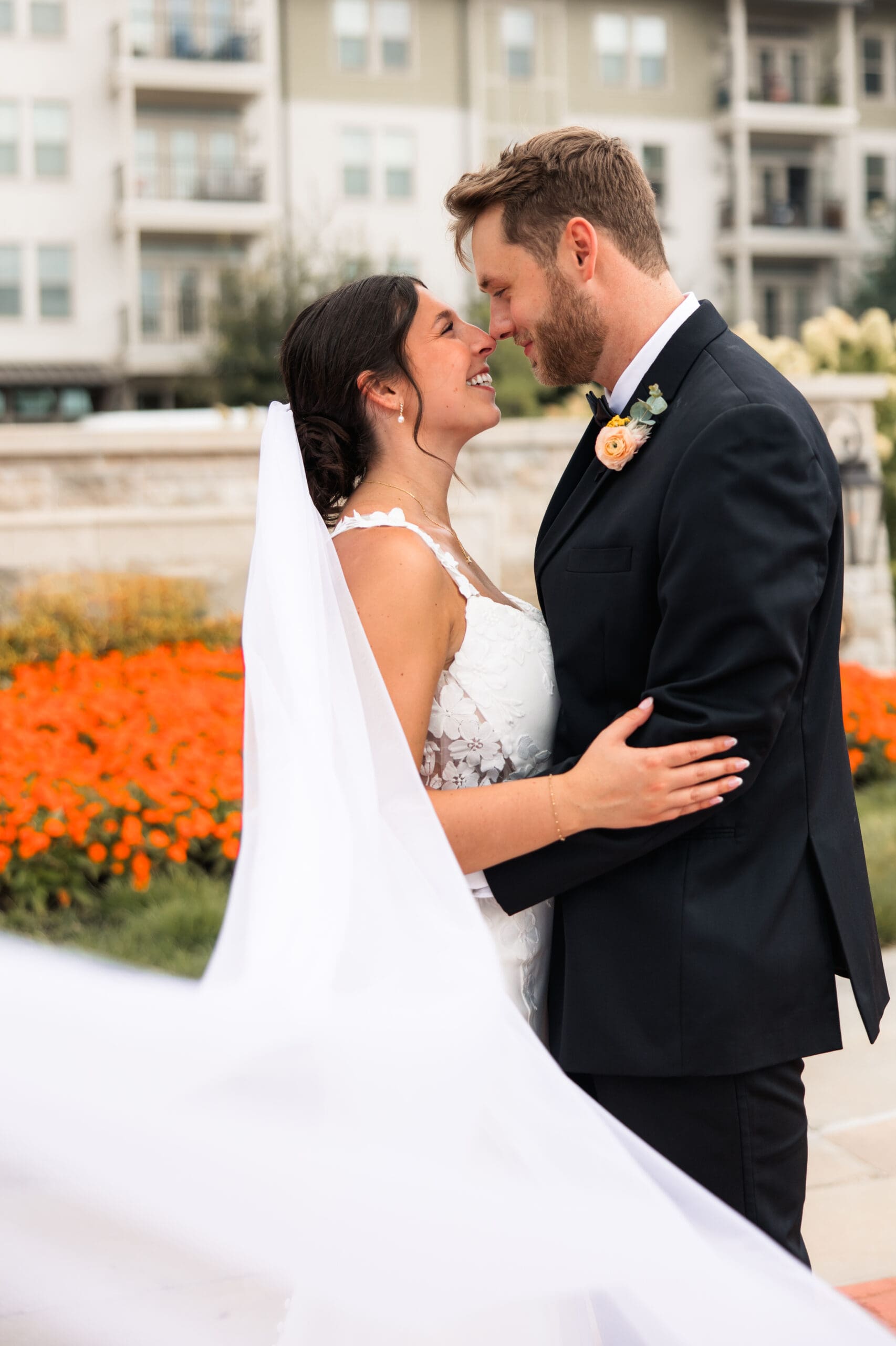Elegant wedding portrait of the bride and groom standing before The Kessler Residences in Overland Park, with lush gardens and soft natural light