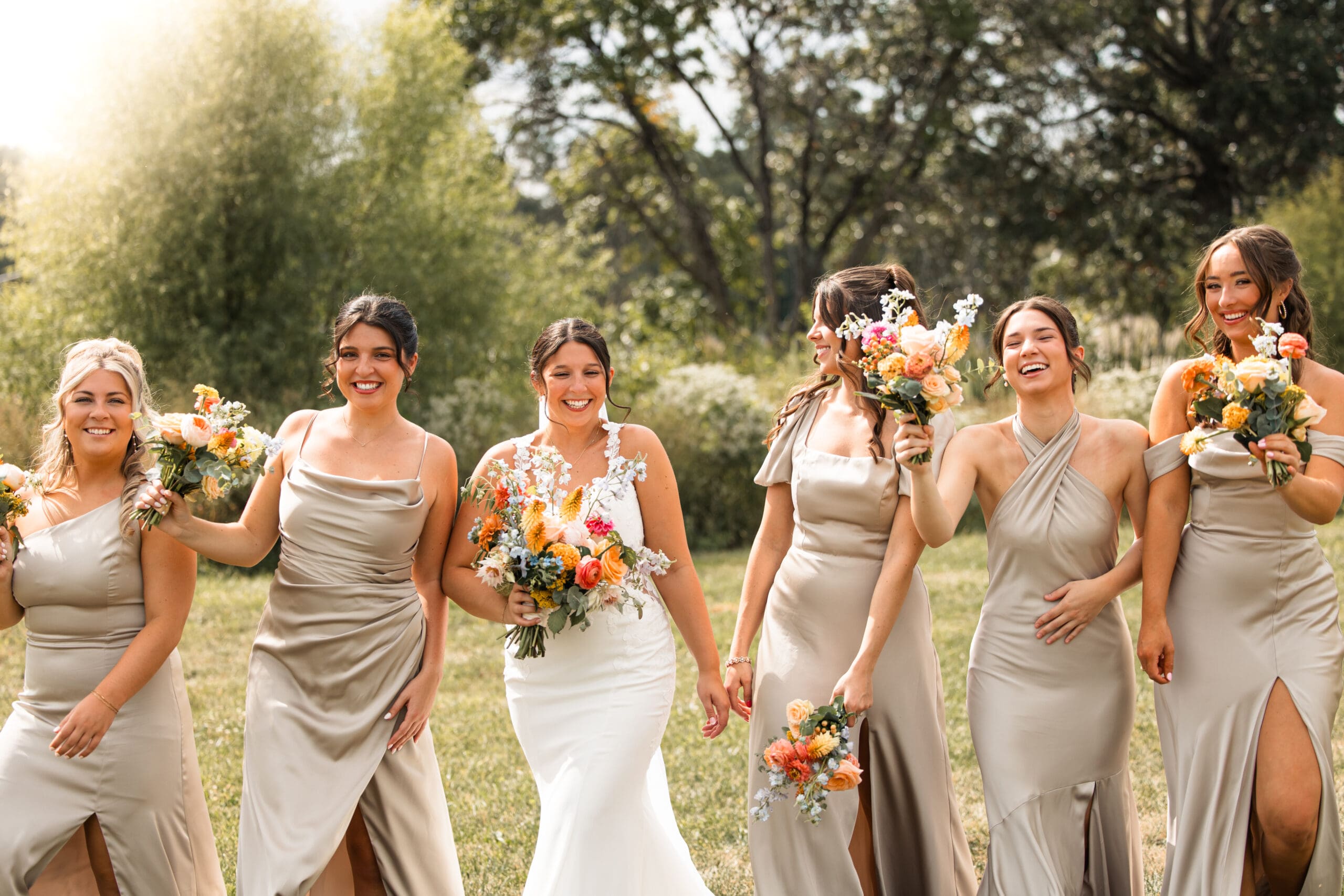 Bride and bridesmaids walking arm-in-arm with colorful bouquets at Meadowbrook Park in Overland Park, photographed by Wichita wedding photographer Briana Jewell Photography