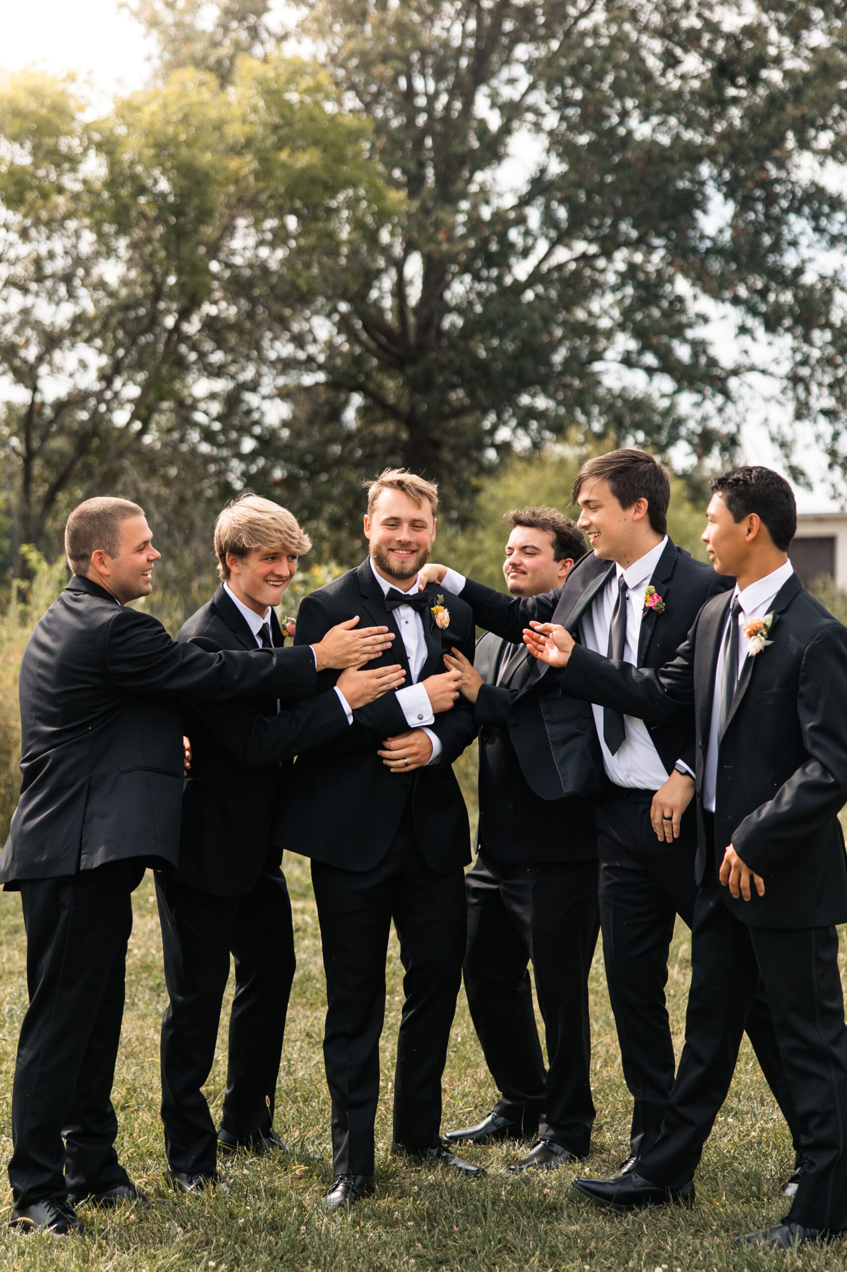 Groom laughing with groomsmen in black tuxedos at Meadowbrook Park in Overland Park, Kansas, captured in timeless editorial style.