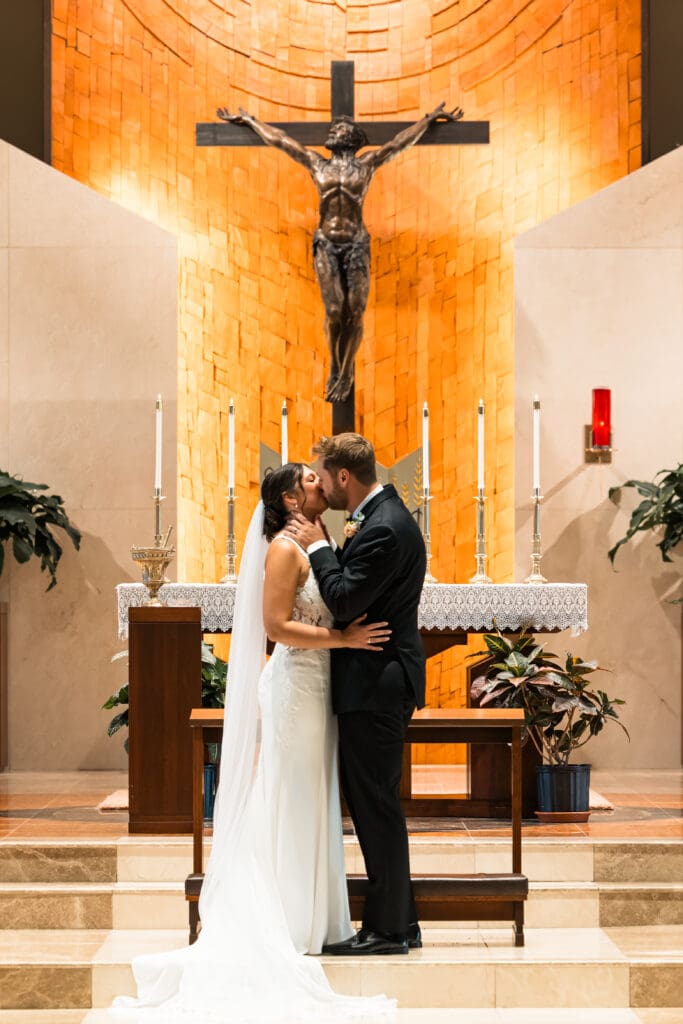 Bride and groom share their first kiss as husband and wife beneath the cross at Holy Spirit Catholic Parish in Overland Park