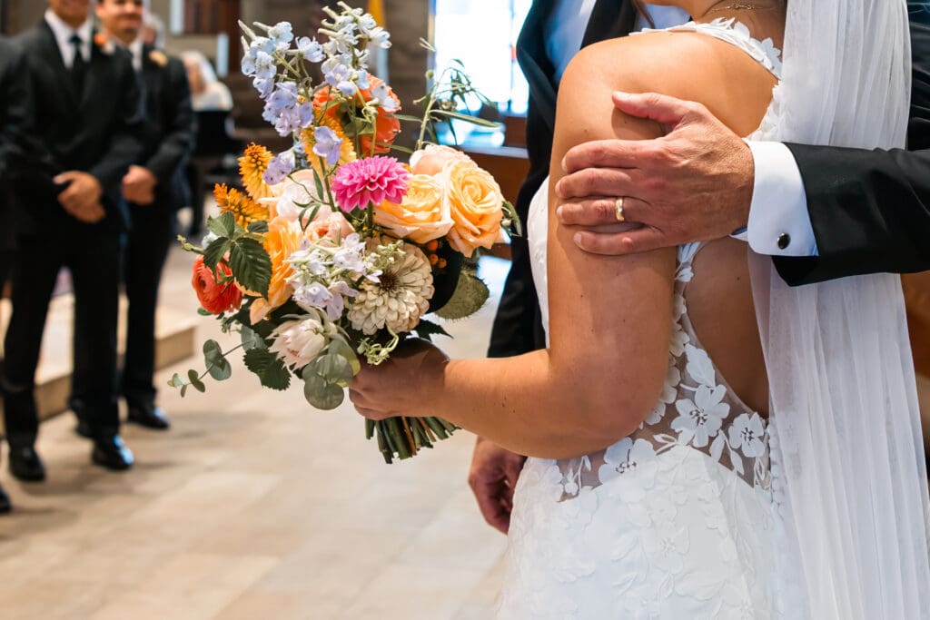 Colorful bridal bouquet with dahlias, roses, and pastel florals during the ceremony at Holy Spirit Catholic Parish in Overland Park, Kansas.