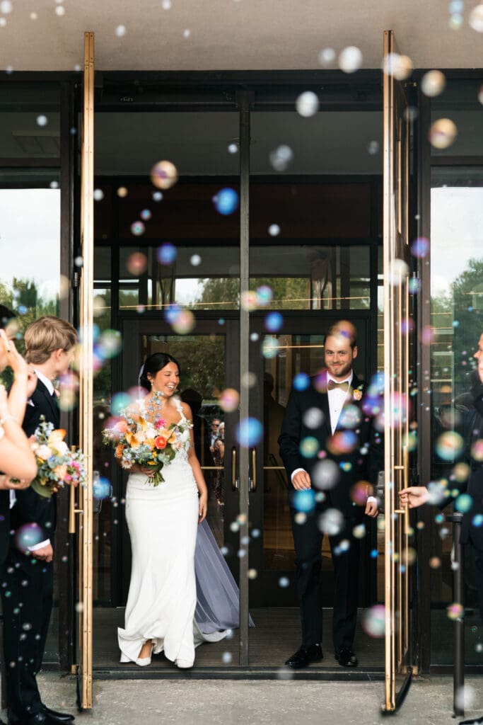 Bride and groom exit Holy Spirit Catholic Parish through a joyful bubble send-off surrounded by cheering guests, captured by Kansas wedding photographer Briana Jewell Photography