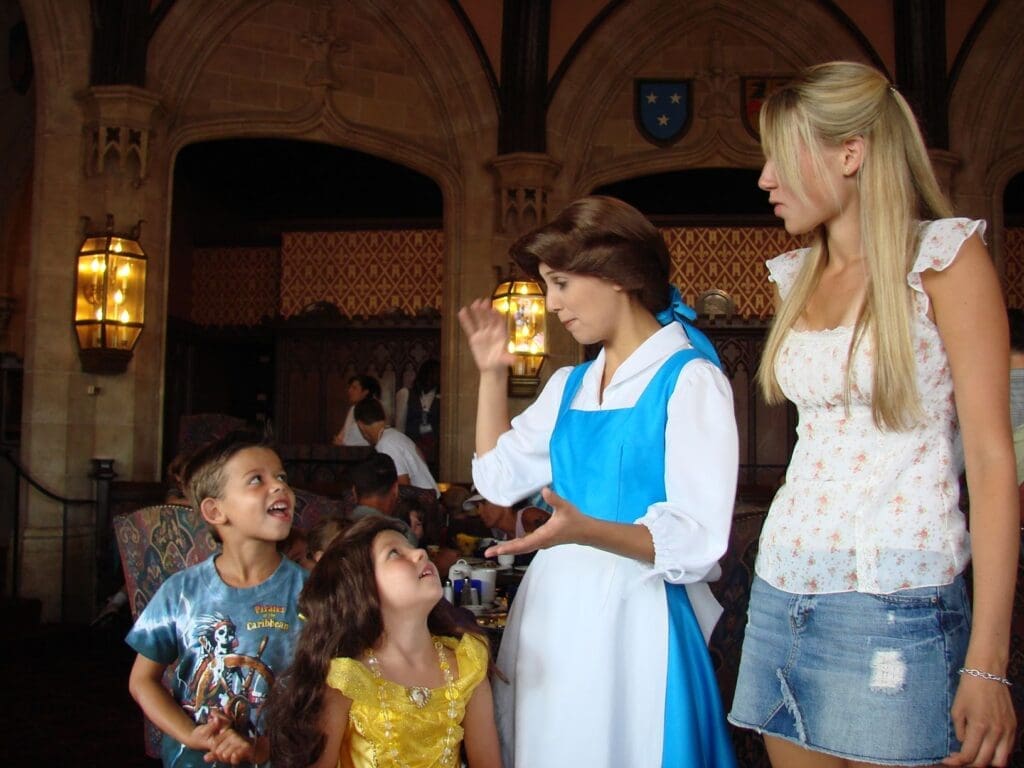 Belle in blue dress gently interacting with young girl in yellow Belle gown at Cinderella’s Castle Disney World – cherished fairy-tale moment from childhood trip