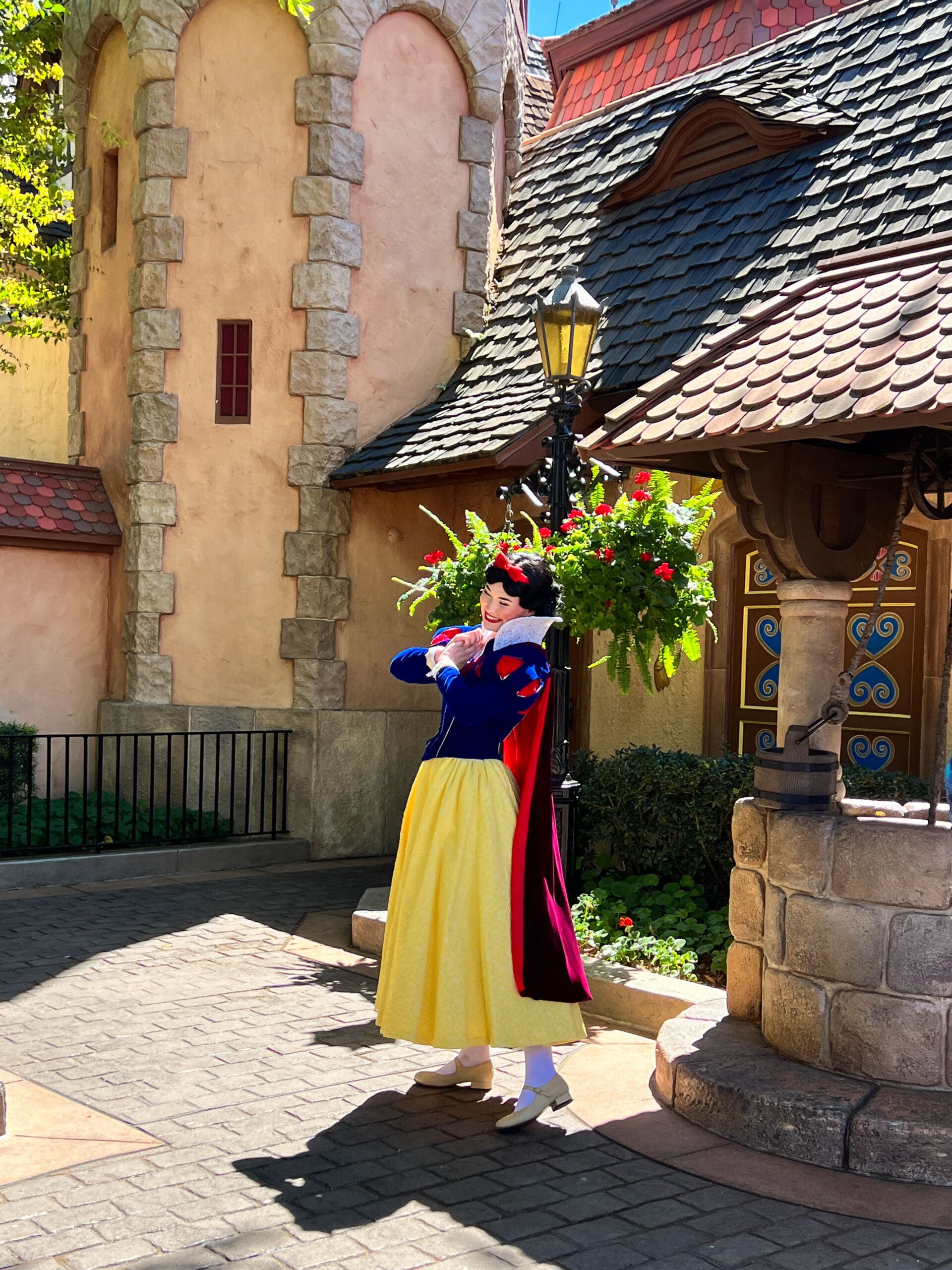 Snow White in classic red, blue, and yellow dress posing in charming stone courtyard at Magic Kingdom Disney World – fairy-tale meet-and-greet magic in Orlando