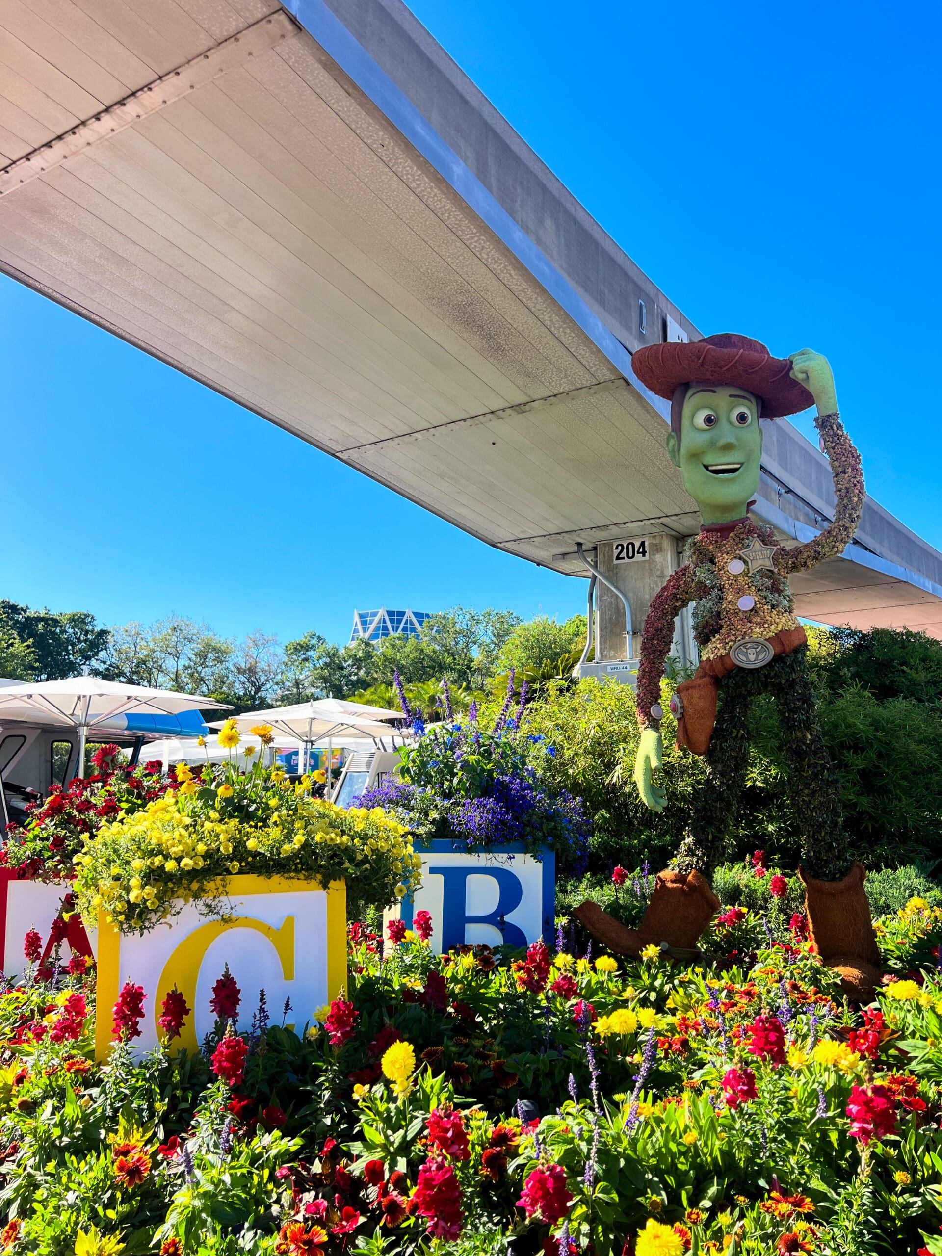 Toy Story's Woody topiary in cowboy hat and boots next to colorful ABC flower beds at Epcot Flower & Garden Festival Disney World – playful Disney character topiary in Orlando