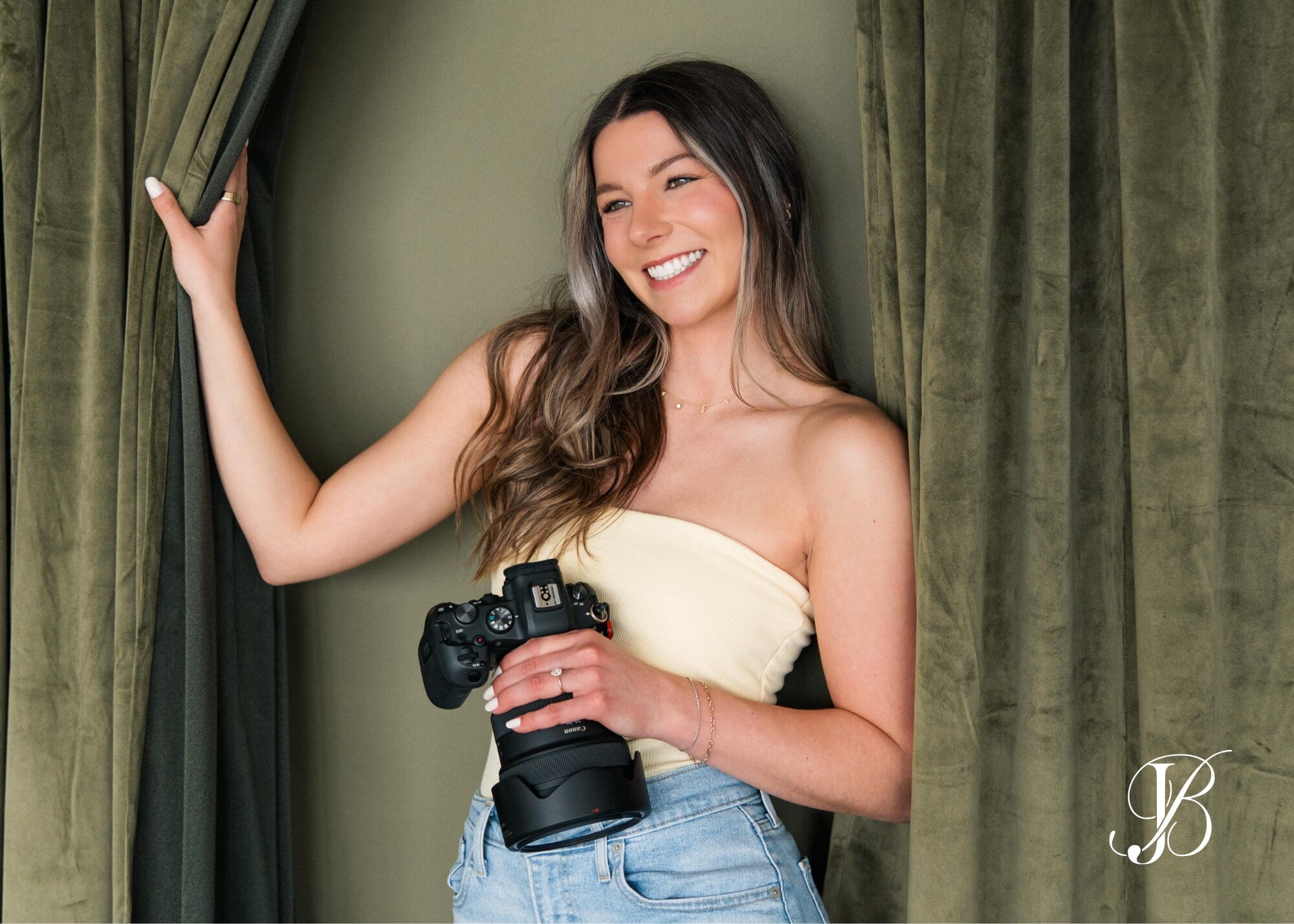 Wichita Kansas wedding photographer Briana smiling with Canon camera against olive green curtains