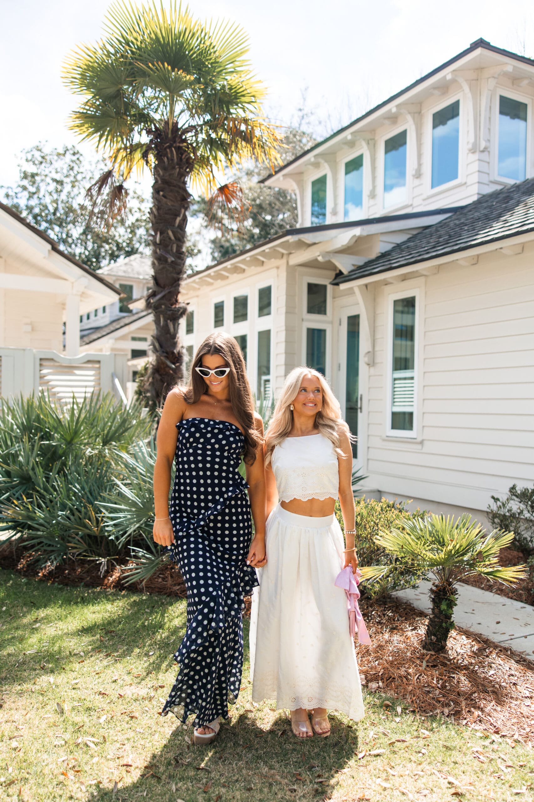Two models walking together in a navy polka dot dress and white eyelet two-piece set during the Fairhope Alabama photoshoot with Ave & Liv