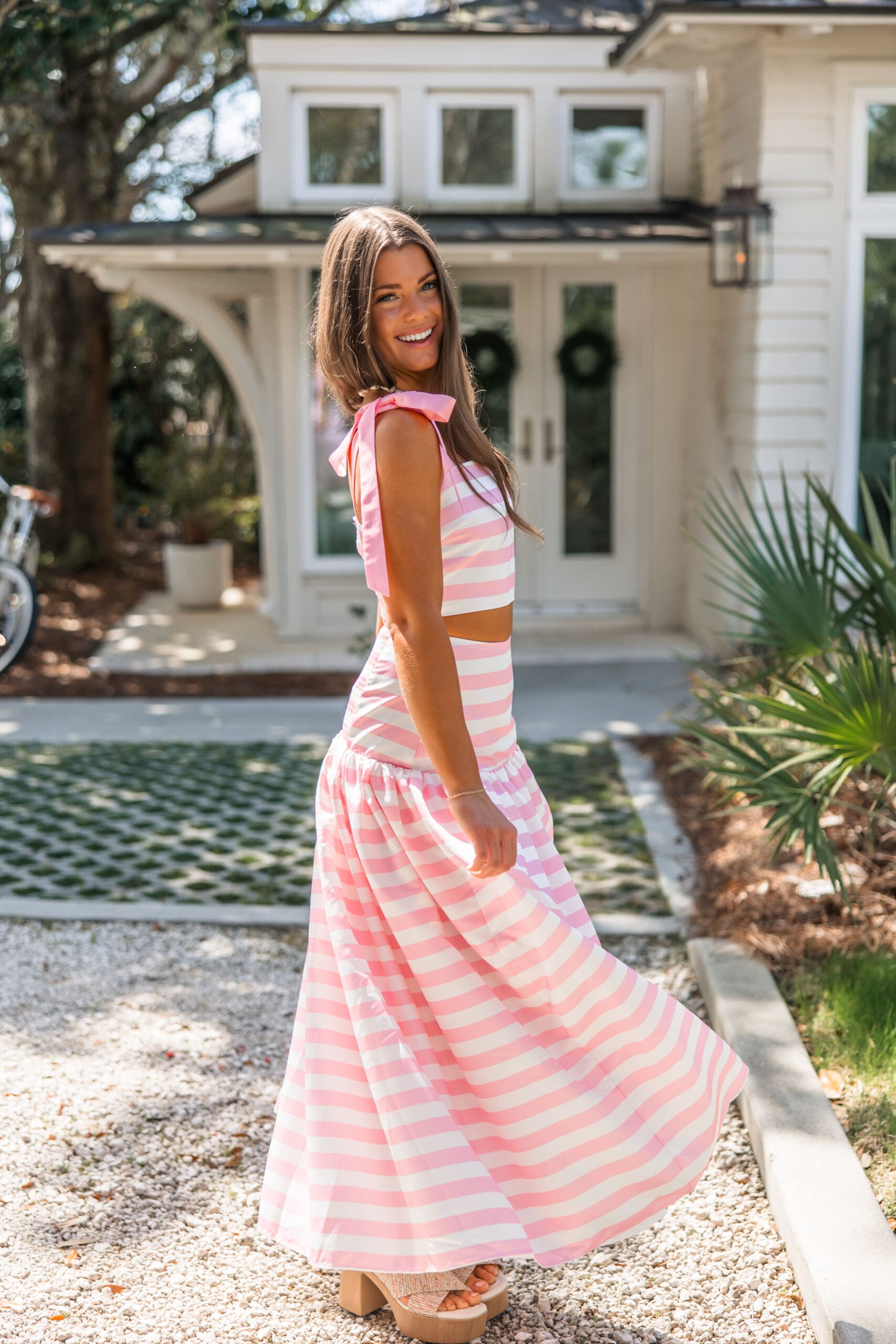 Model smiling in a pink and white striped bow-shoulder crop top and tiered maxi skirt from Ave & Liv during the Fairhope Alabama photoshoot at Lucia Bleu Cottages