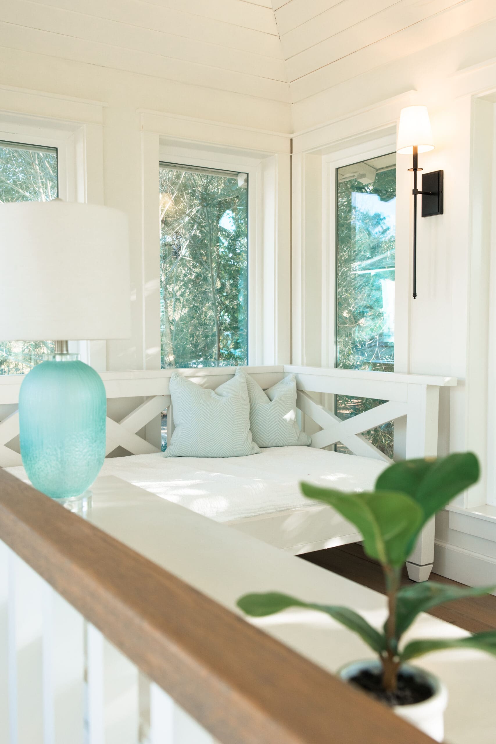 Cozy white daybed with herringbone pillows and turquoise glass lamp inside Lucia Bleu Fairhope Cottages, captured during a Fairhope Alabama photoshoot, overlooking lush greenery