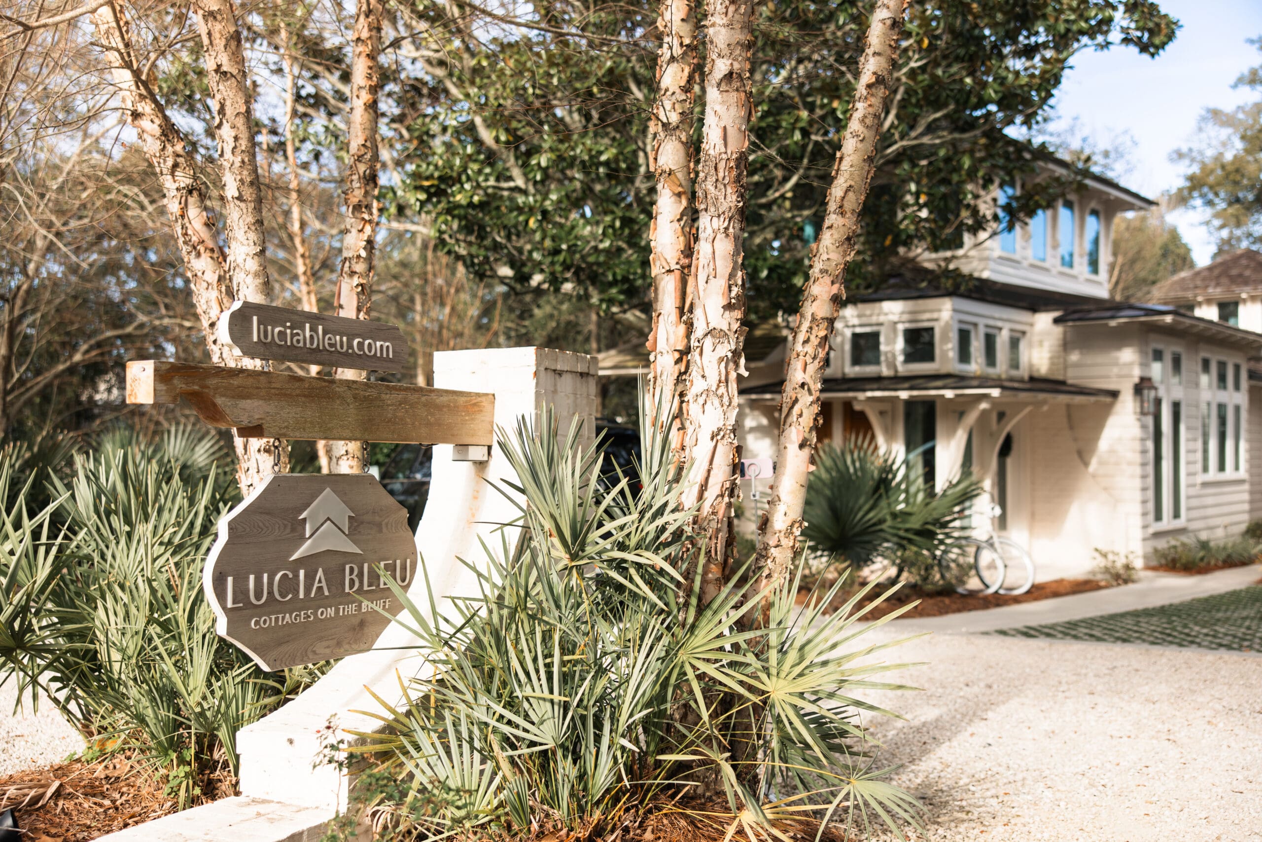 Lucia Bleu Cottages on the Bluff entrance sign reading luciableu.com during the Fairhope Alabama photoshoot, with the luxury white cottages visible through the trees