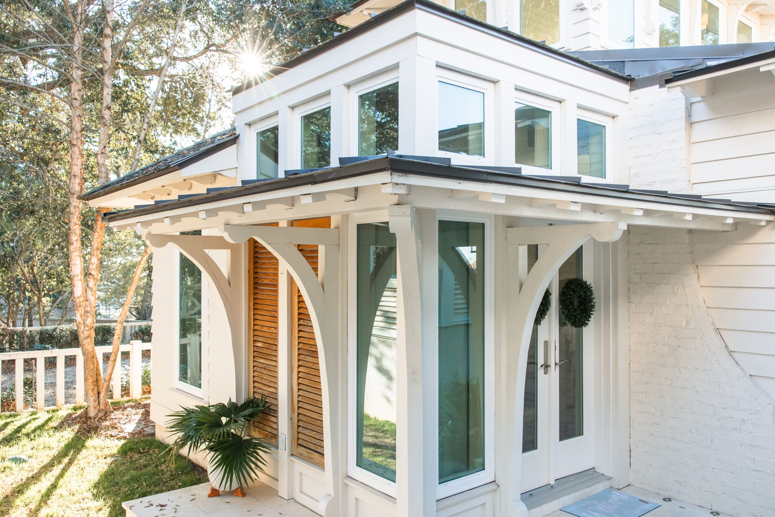 Bright sunlight streaming over the white architecture and wooden shutters of Lucia Bleu Fairhope Cottages during a Fairhope Alabama photoshoot, creating a dreamy golden glow