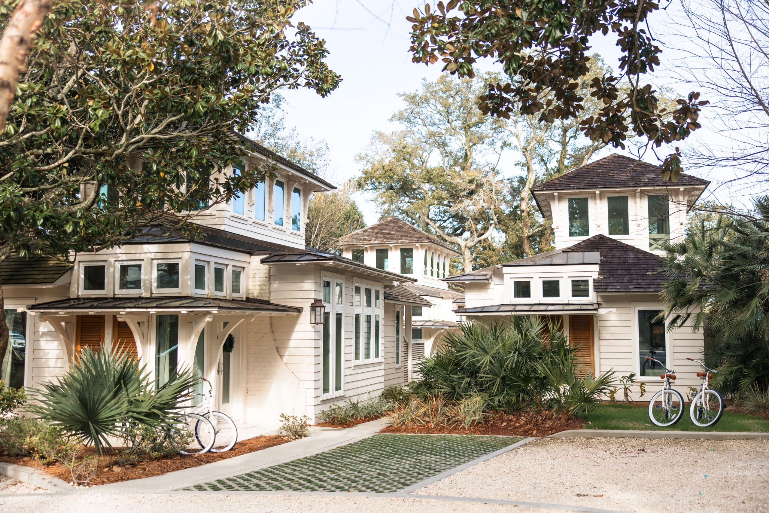 Overview of the beautiful white Lucia Bleu Fairhope Cottages nestled among magnolia trees and palm plants during a Fairhope Alabama photoshoot, with white cruiser bicycles parked outside