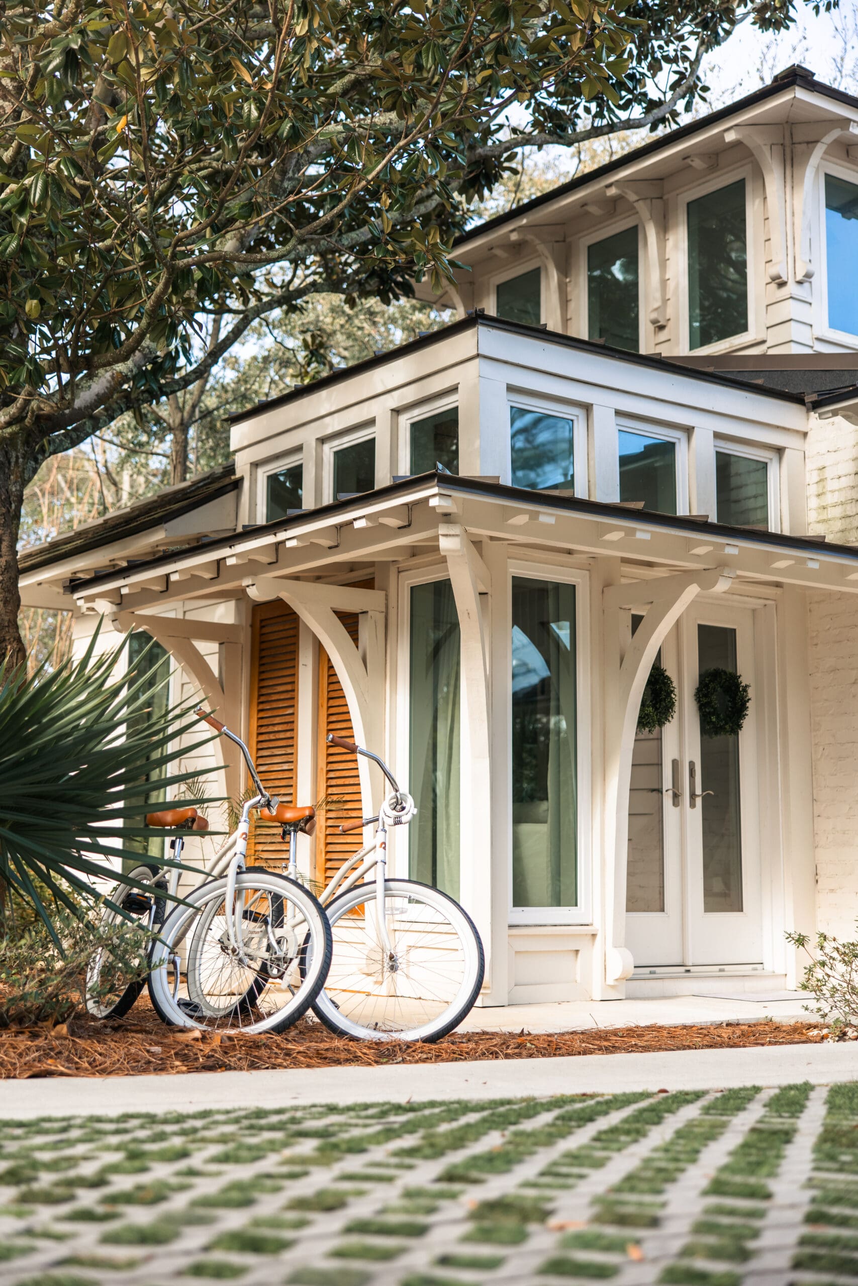 White cruiser bicycles parked in front of the elegant Lucia Bleu Fairhope Cottages with palm fronds in the foreground during a Fairhope Alabama photoshoot