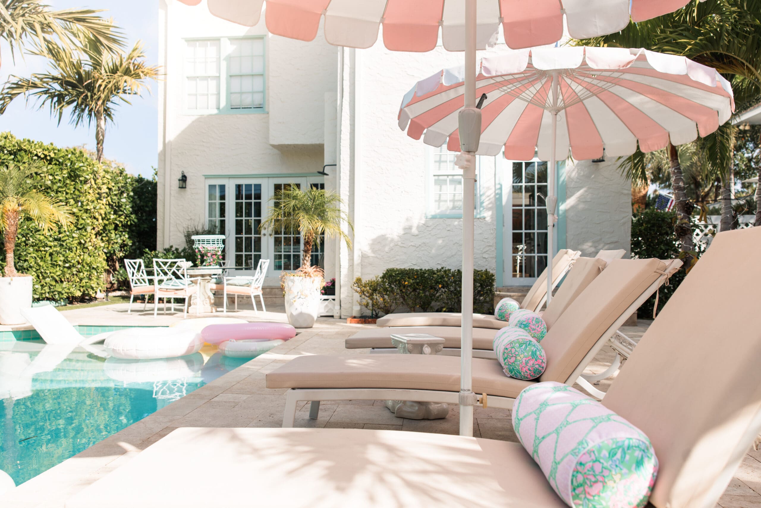 Pink-and-white striped umbrellas and colorful pool floats at The Pink Palm Beach saltwater pool – dreamy girly setup for Pink Palm Beach bachelorette getaway