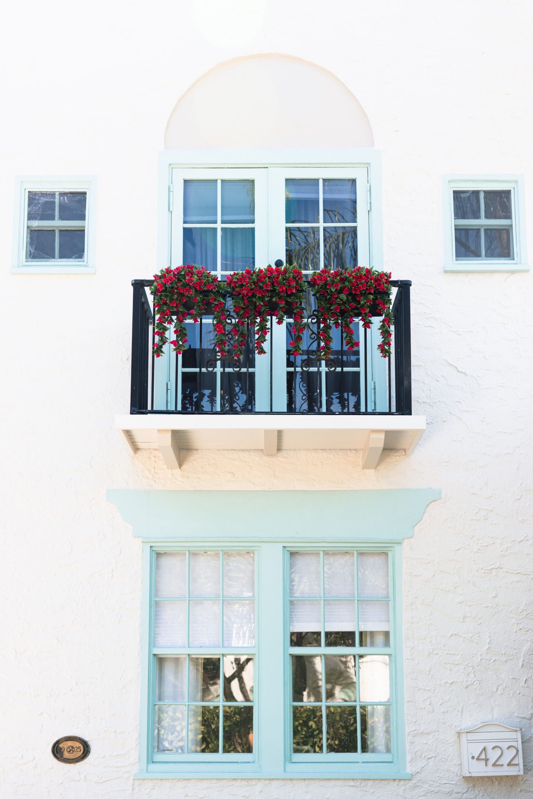 Mint-green arched balcony with red flowering vines and house number 422 at The Pink Palm Beach cottages – feminine elegance in historic Old Northwood