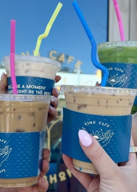 Three iced coffee drinks with colorful straws from The Kind Cafe in Fairhope, Alabama during a Fairhope Alabama photoshoot, featuring the honey cinnamon latte and signature blue sleeves